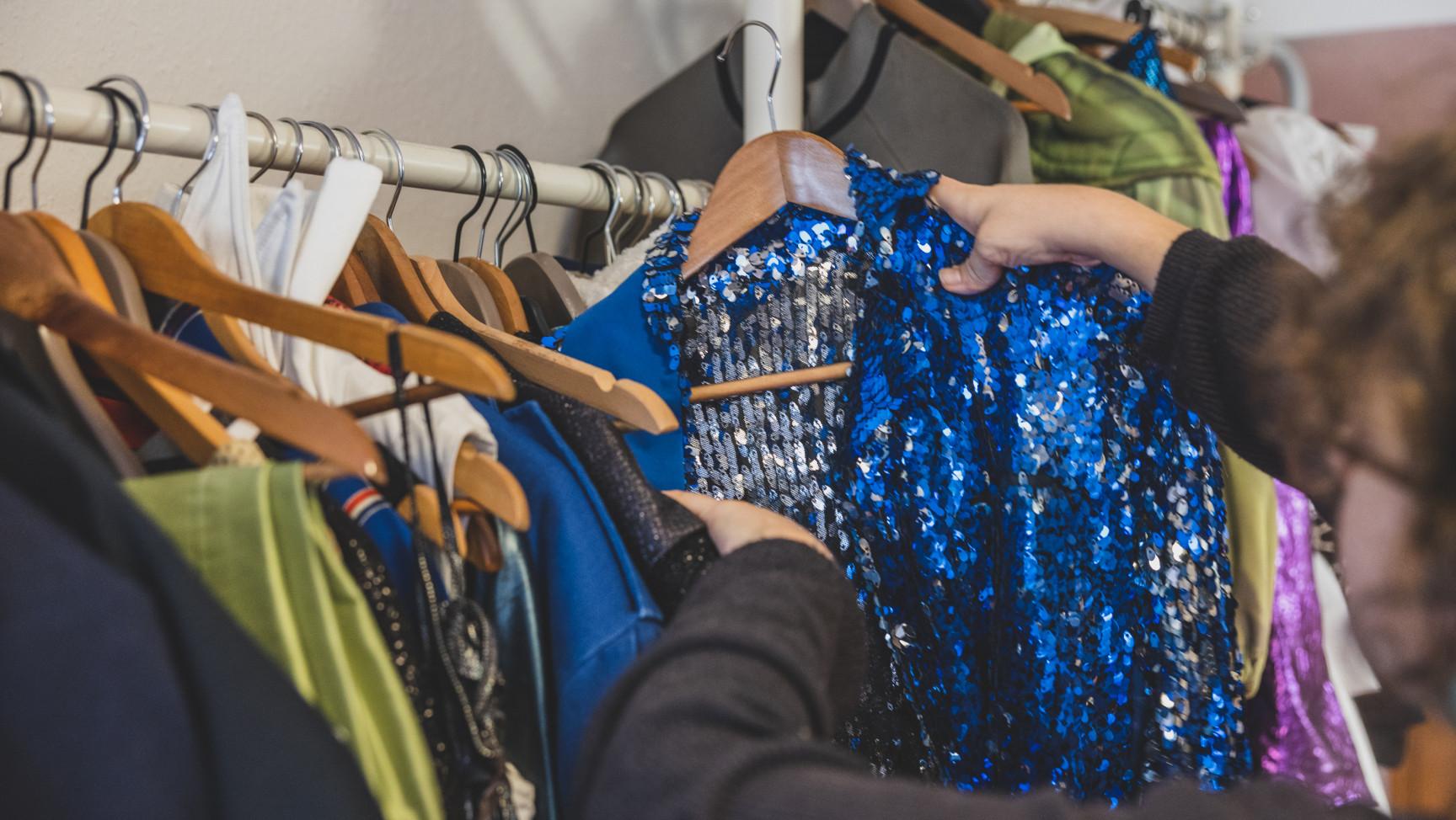 eine Person nimmt eine Jacke mit blauen Pailetten von einer Kleiderstange