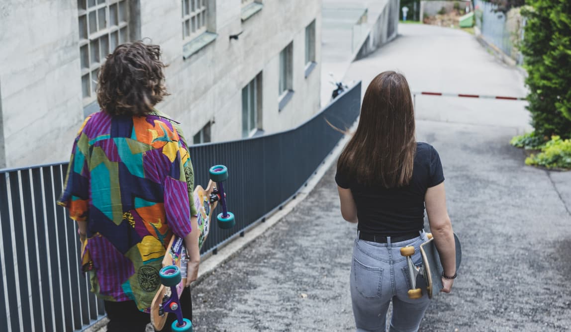 Zwei Jugendliche laufen mit den Skateboards in der Hand eine Straße hinunter.