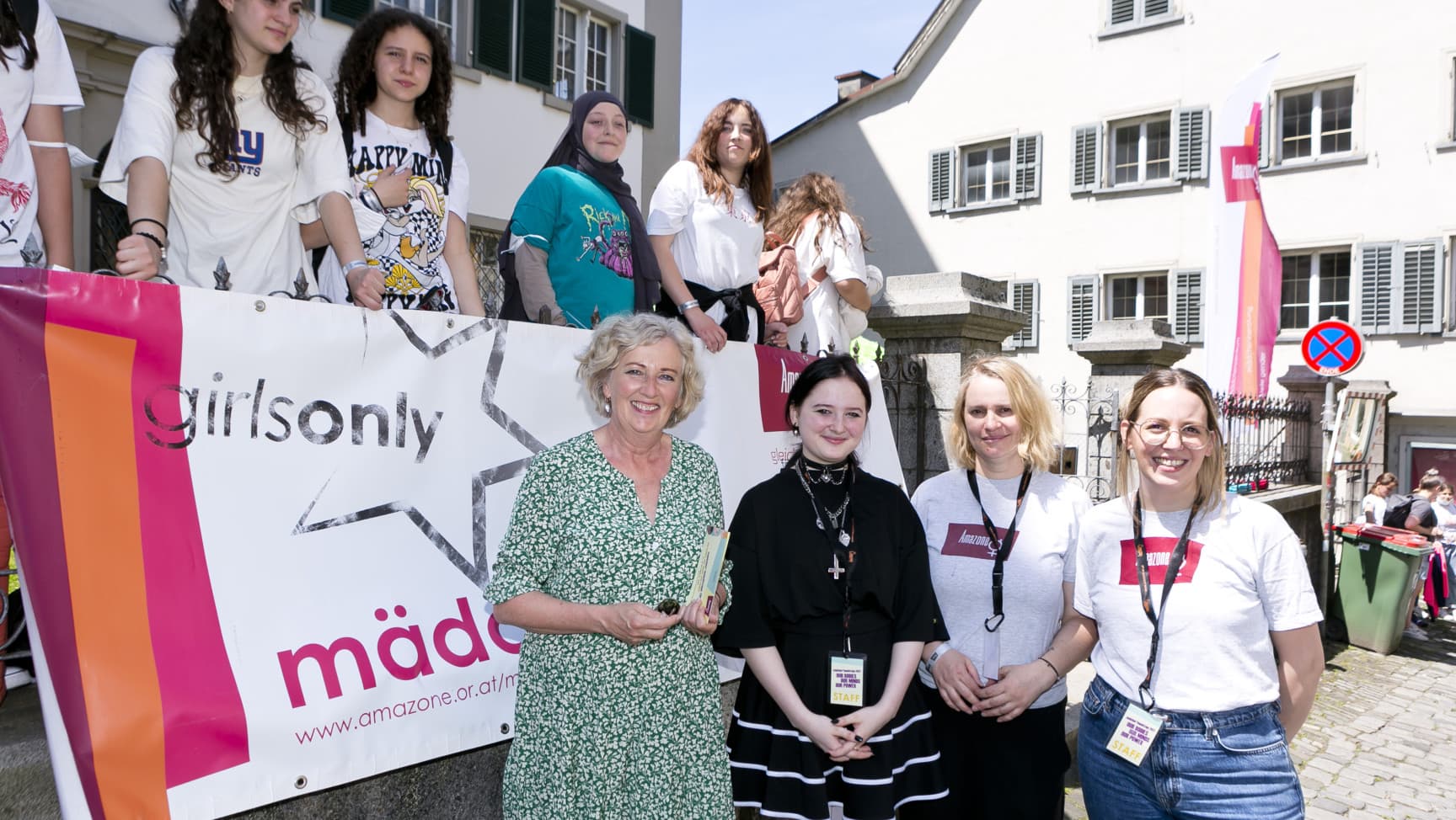 Landesrätin, Mitarbeiterinnen* und Besucherinnen* vor einem Banner