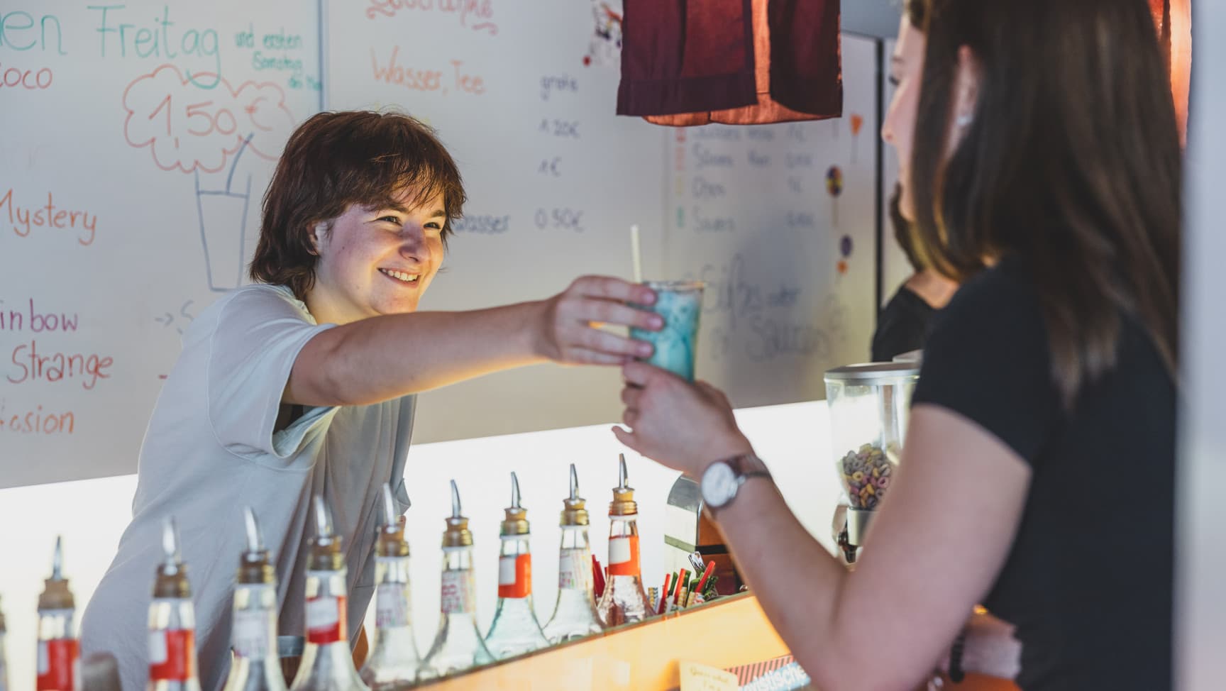 Eine jugendliche Person reicht einer anderen Person einen Drink über die Bar.